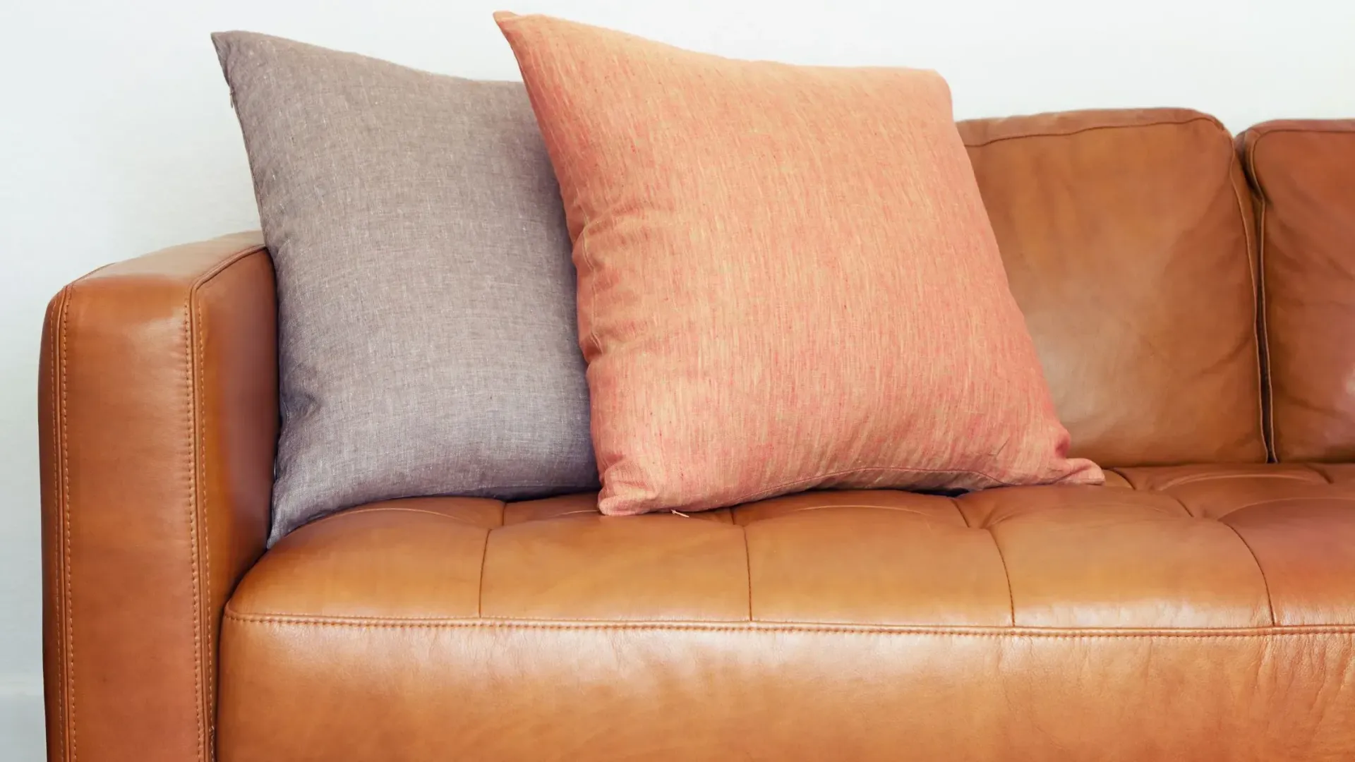 Light brown leather couch with two pillows leaning at the end.