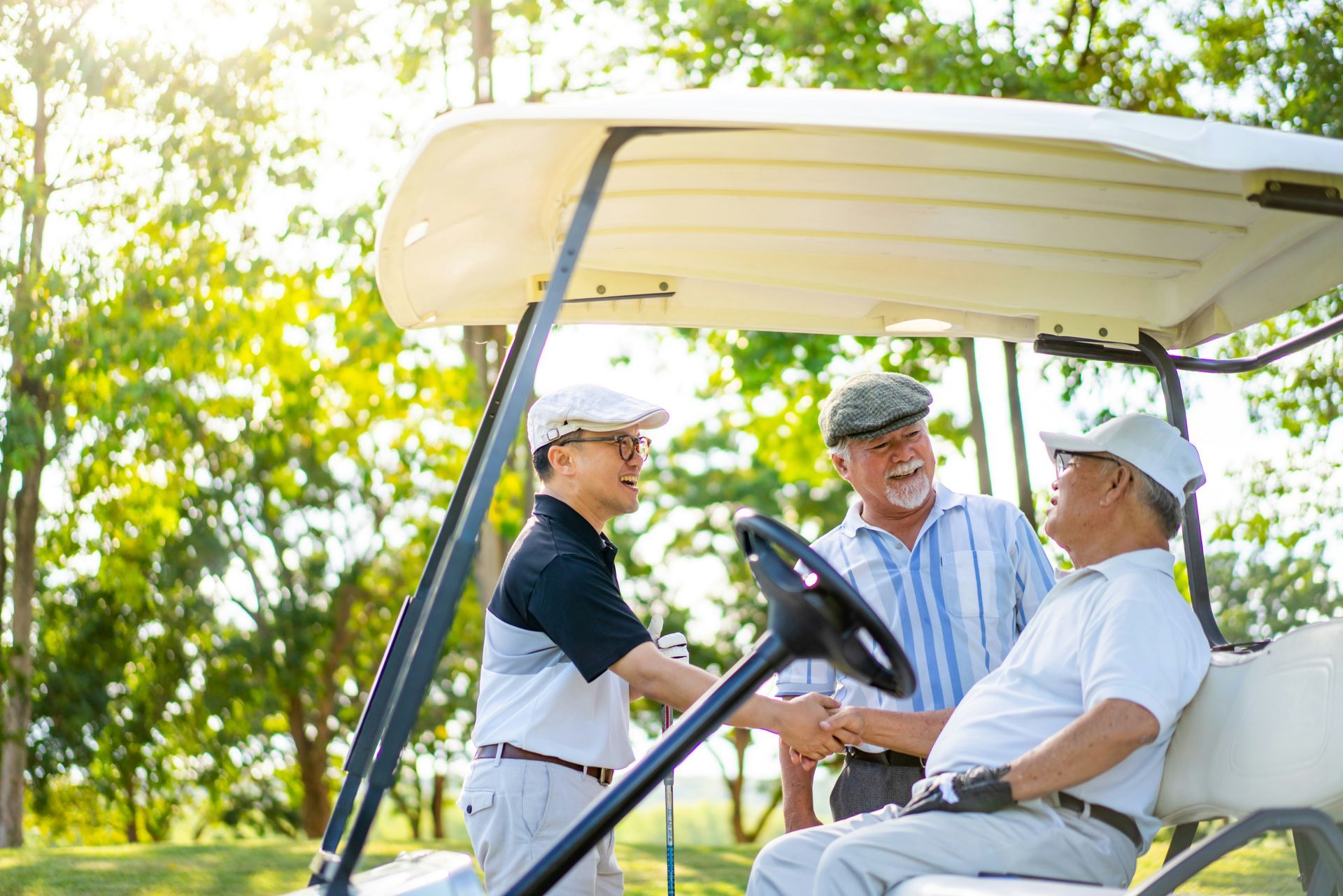 Three older men are shaking hands while sitting in a golf cart on a golf course.
