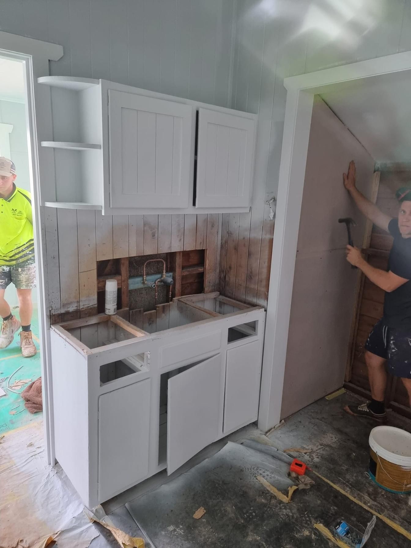A Man Is Working On A Kitchen With White Cabinets And A Sink — LMS Painting & Maintenance Pty Ltd In Singleton, NSW
