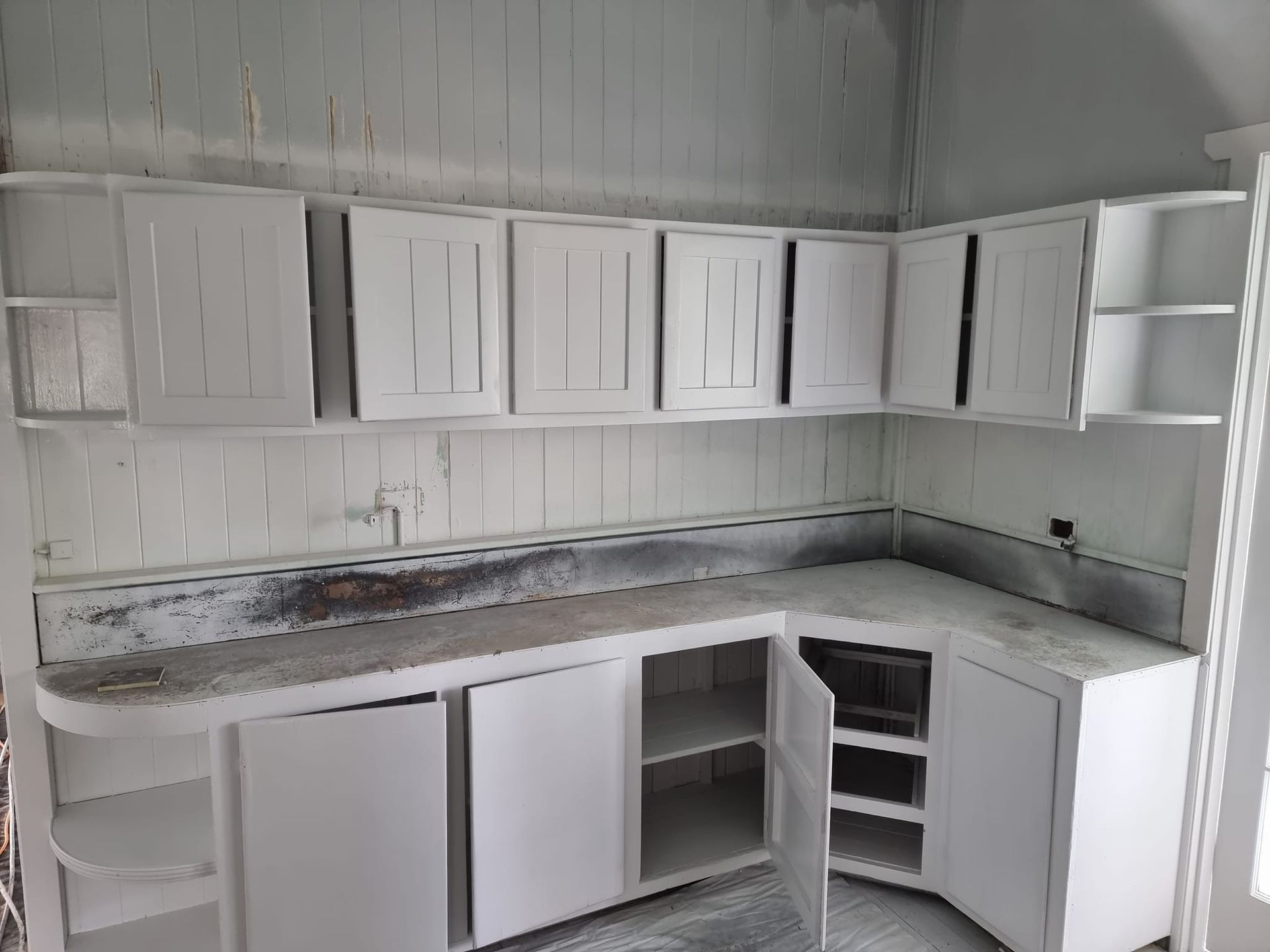 An Empty Kitchen With White Cabinets And Shelves — LMS Painting & Maintenance Pty Ltd In North Lambton, NSW