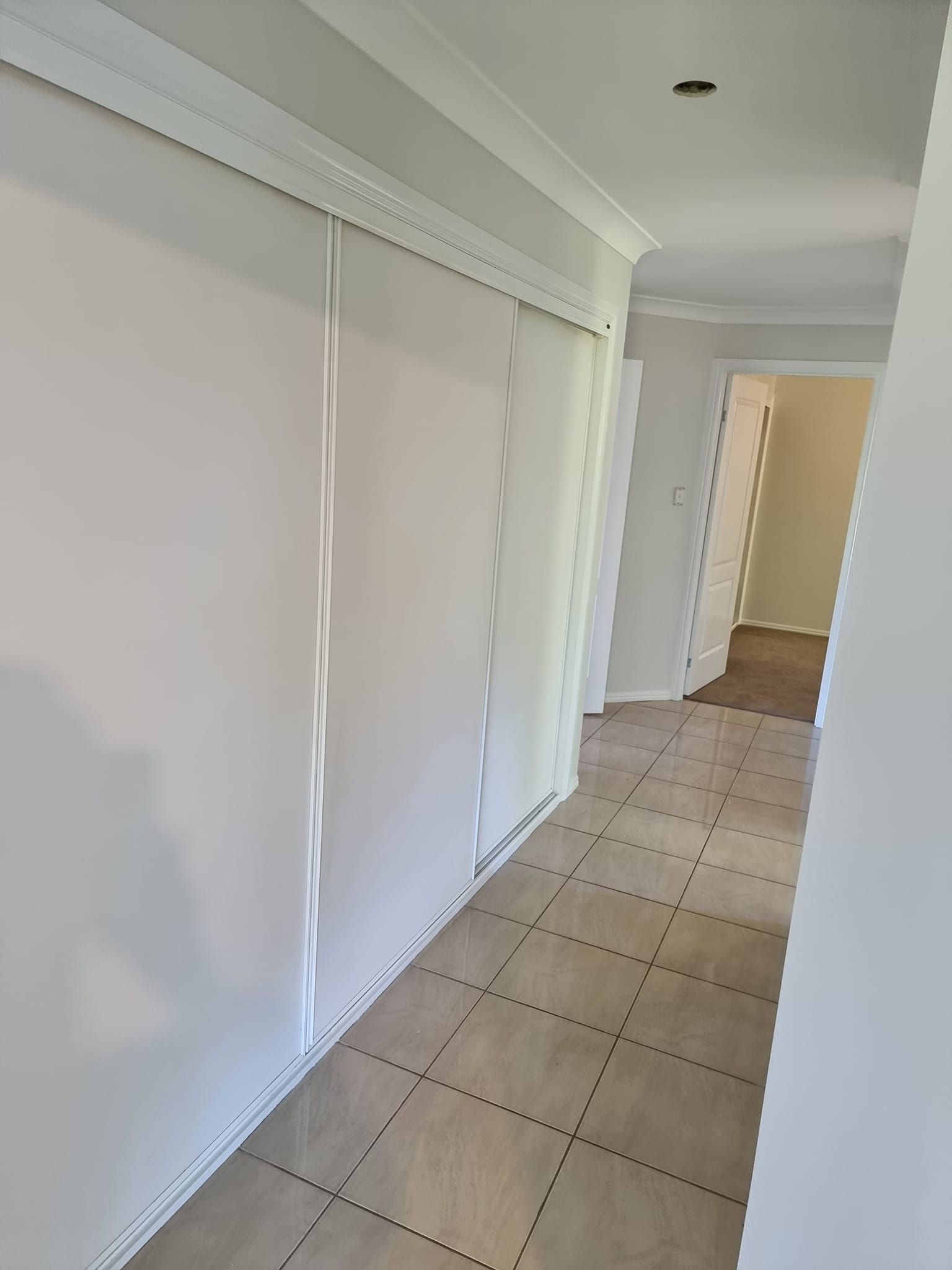 A Long Hallway With White Walls And Tile Floors In A House — LMS Painting & Maintenance Pty Ltd In Swansea, NSW