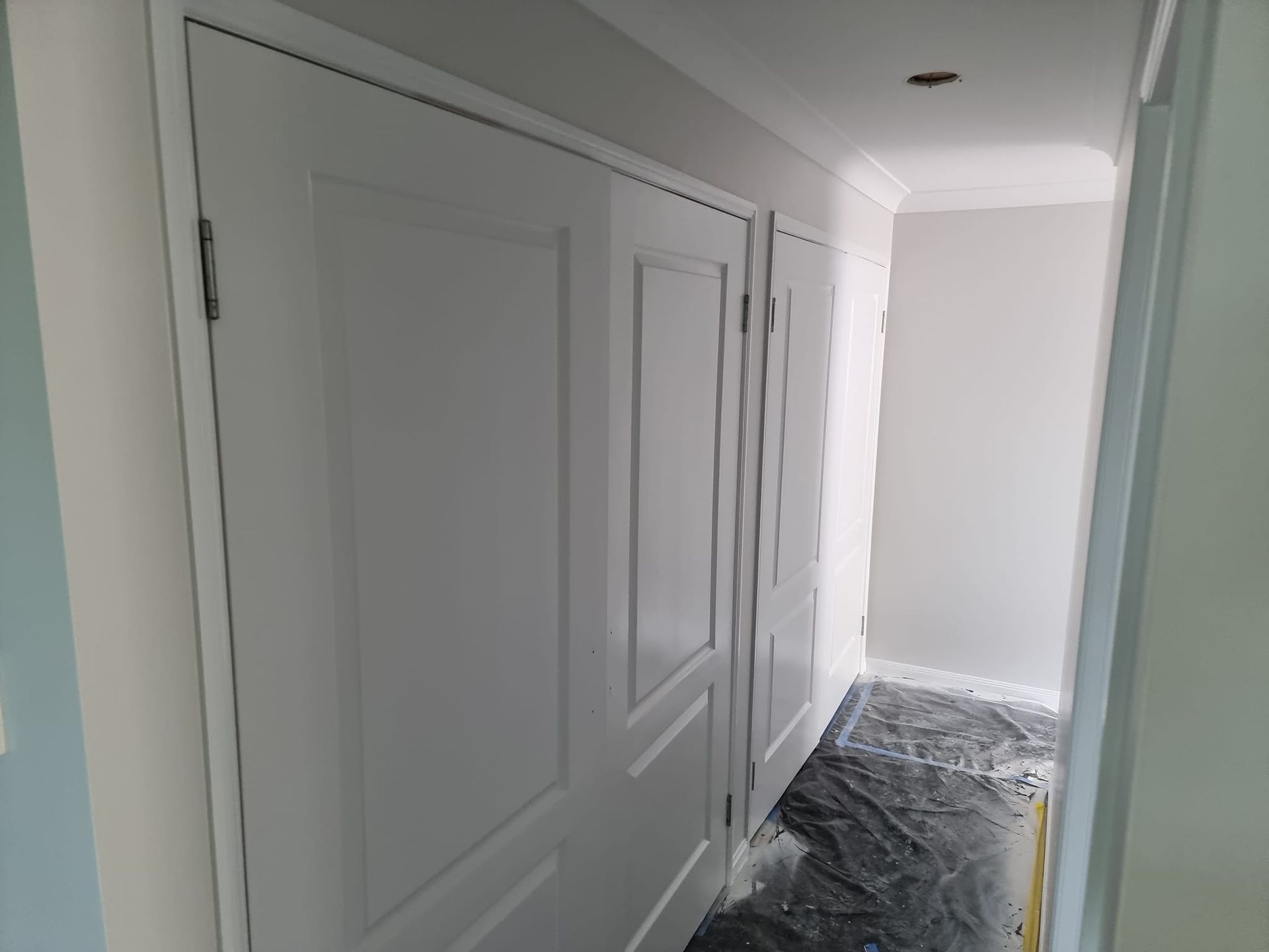 A Hallway With White Doors And A Black Tarp On The Floor — LMS Painting & Maintenance Pty Ltd In Lake Macquarie, NSW