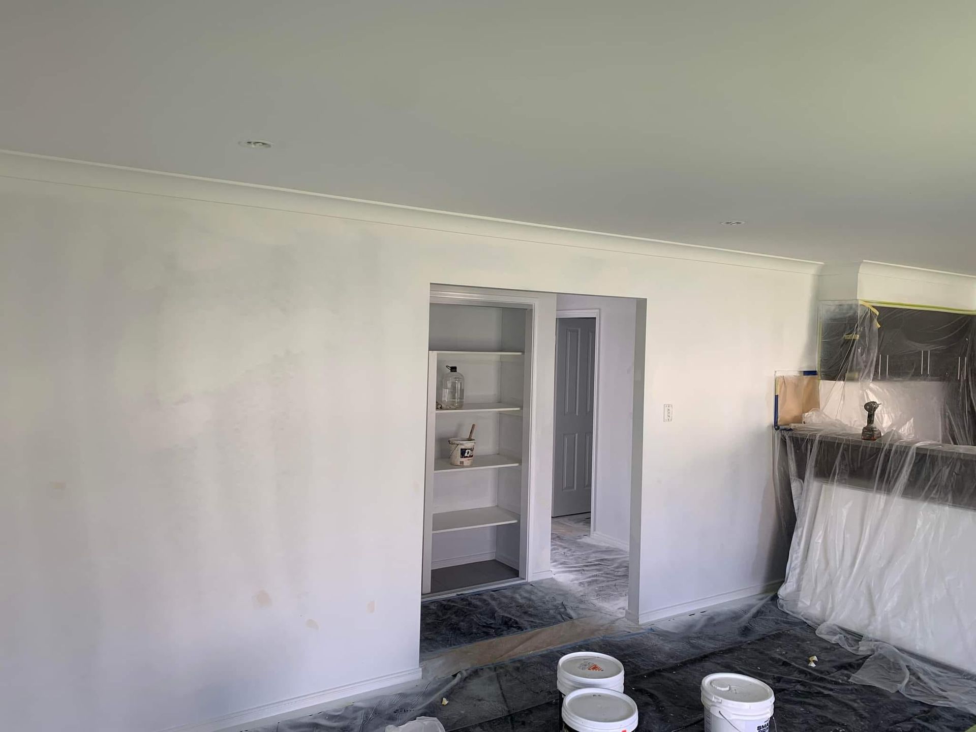 A Living Room Is Being Painted White With Buckets Of Paint — LMS Painting & Maintenance Pty Ltd In Medowie, NSW