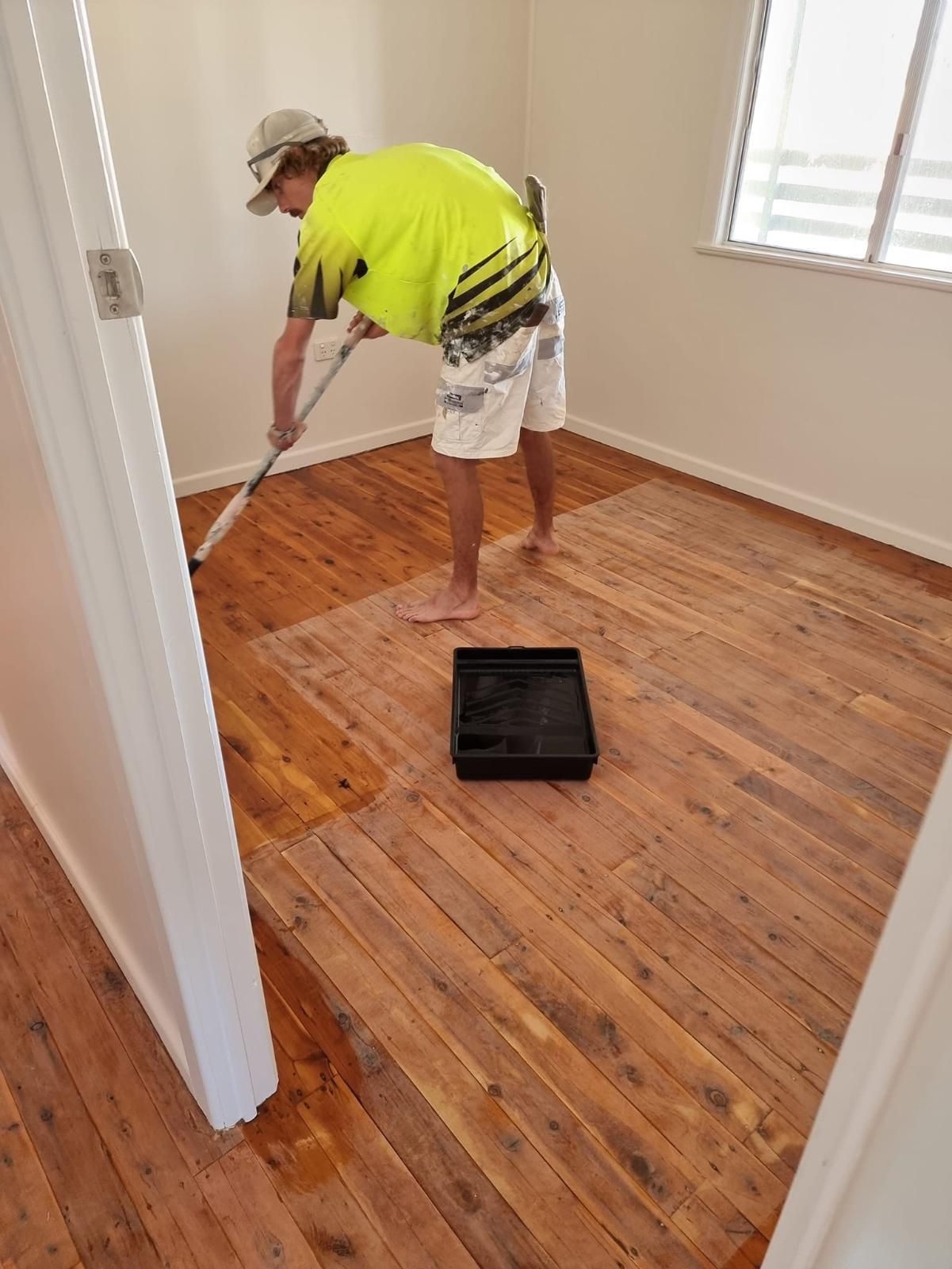 A Man Is Painting A Wooden Floor In A Room — LMS Painting & Maintenance Pty Ltd In North Lambton, NSW