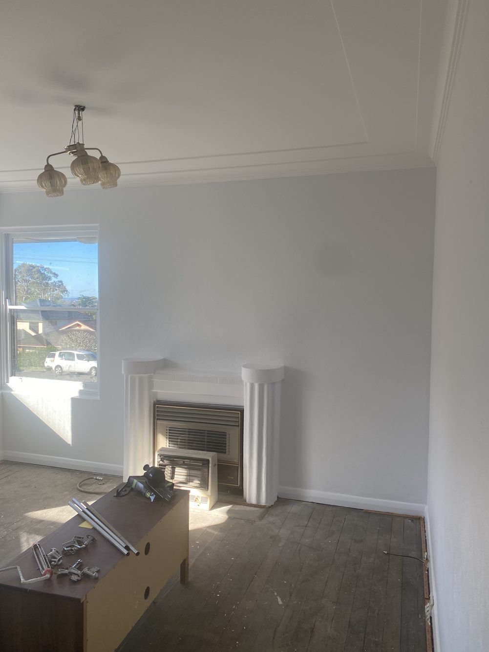 An empty living room with a fireplace and a chandelier — LMS Painting & Maintenance Pty Ltd In North Lambton, NSW