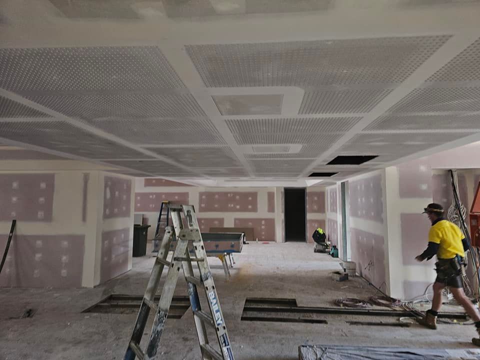 A Man Is Standing Next To A Ladder In A Room Under Construction — LMS Painting & Maintenance Pty Ltd In North Lambton, NSW
