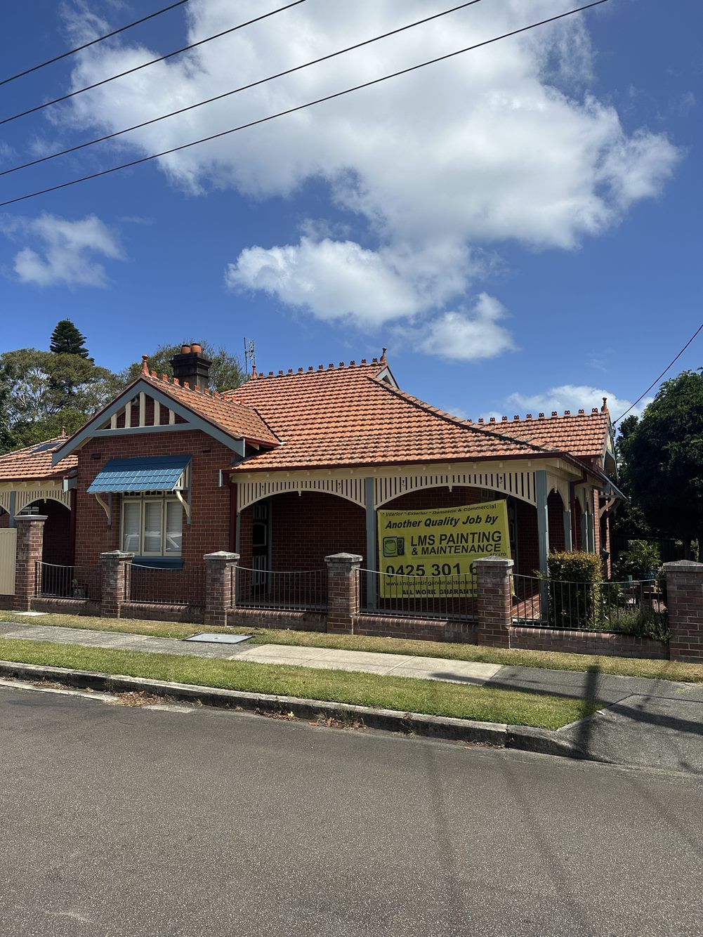 A brick house with a tiled roof and a yellow sign in front of it — LMS Painting & Maintenance Pty Ltd In North Lambton, NSW