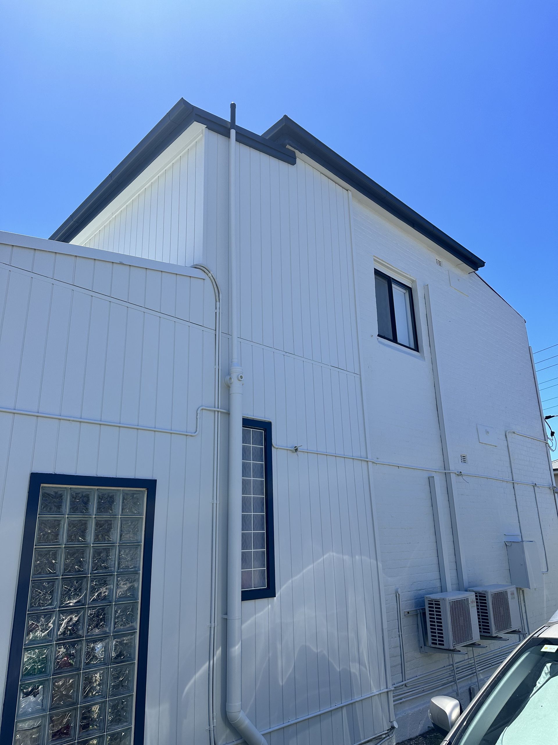 A white building with a blue sky in the background and a car parked in front of it — LMS Painting & Maintenance Pty Ltd In North Lambton, NSW