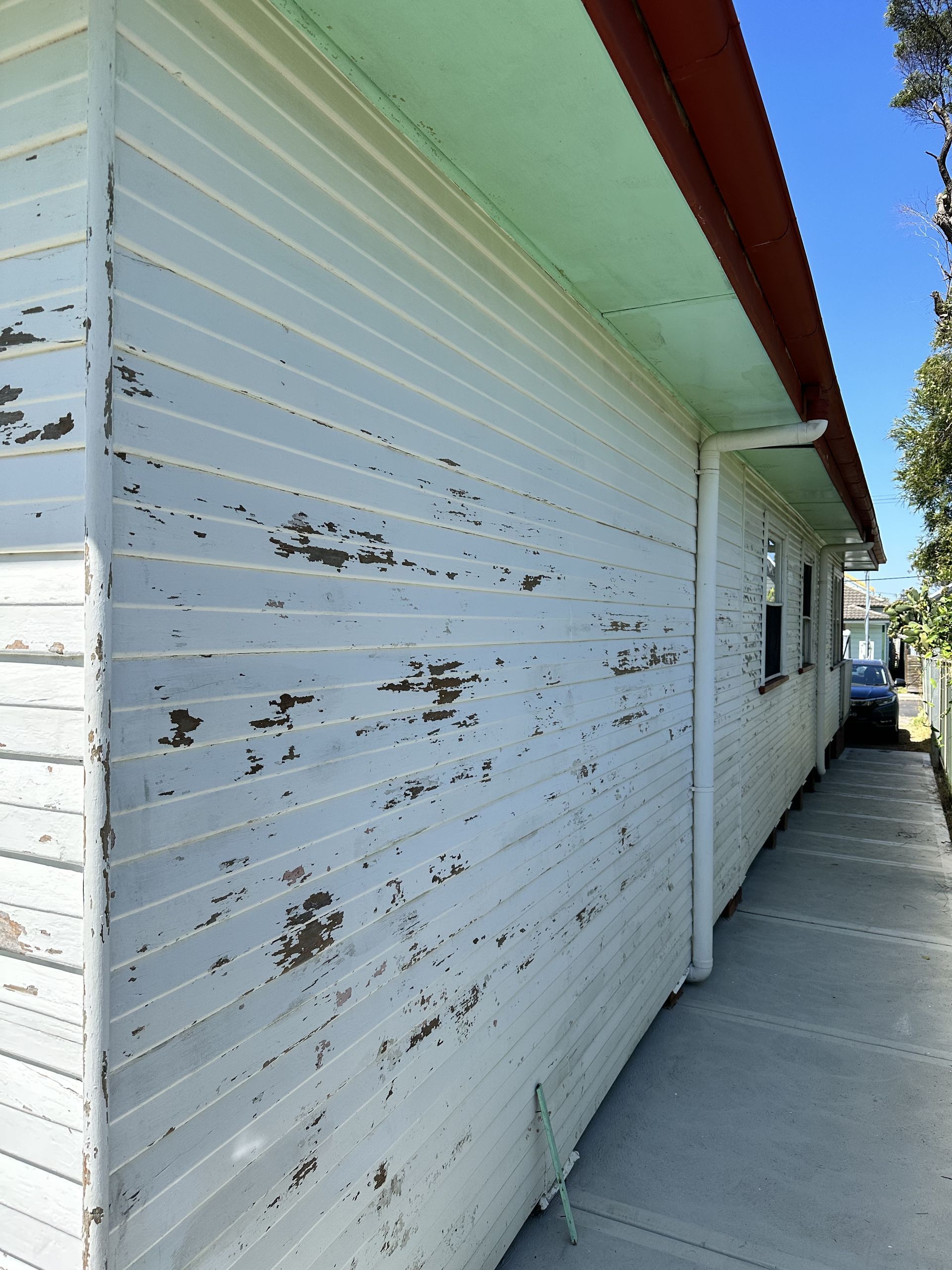 A white house with peeling paint and a red roof — LMS Painting & Maintenance Pty Ltd In North Lambton, NSW