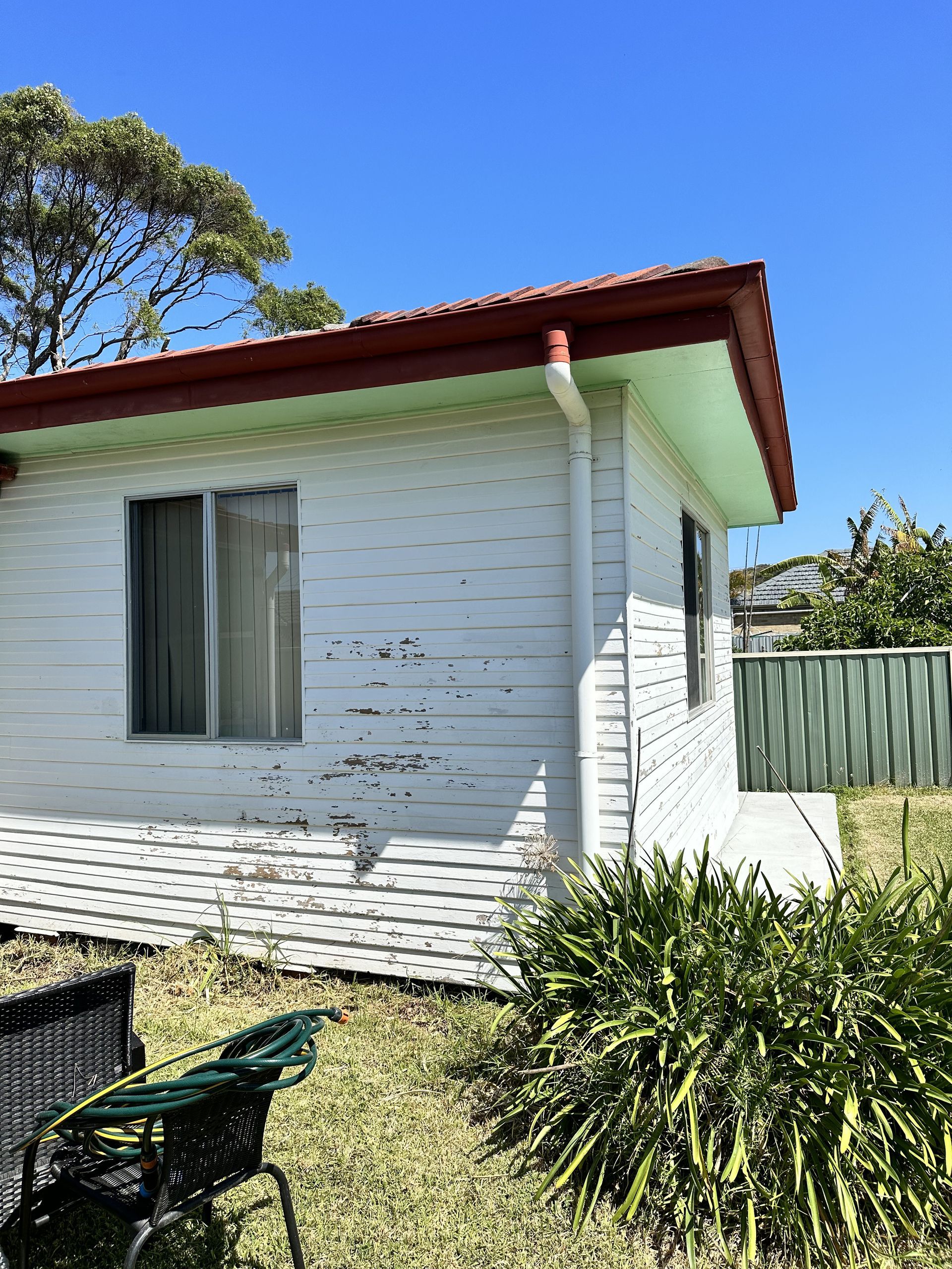 A small white house with a red roof and a green roof — LMS Painting & Maintenance Pty Ltd In North Lambton, NSW