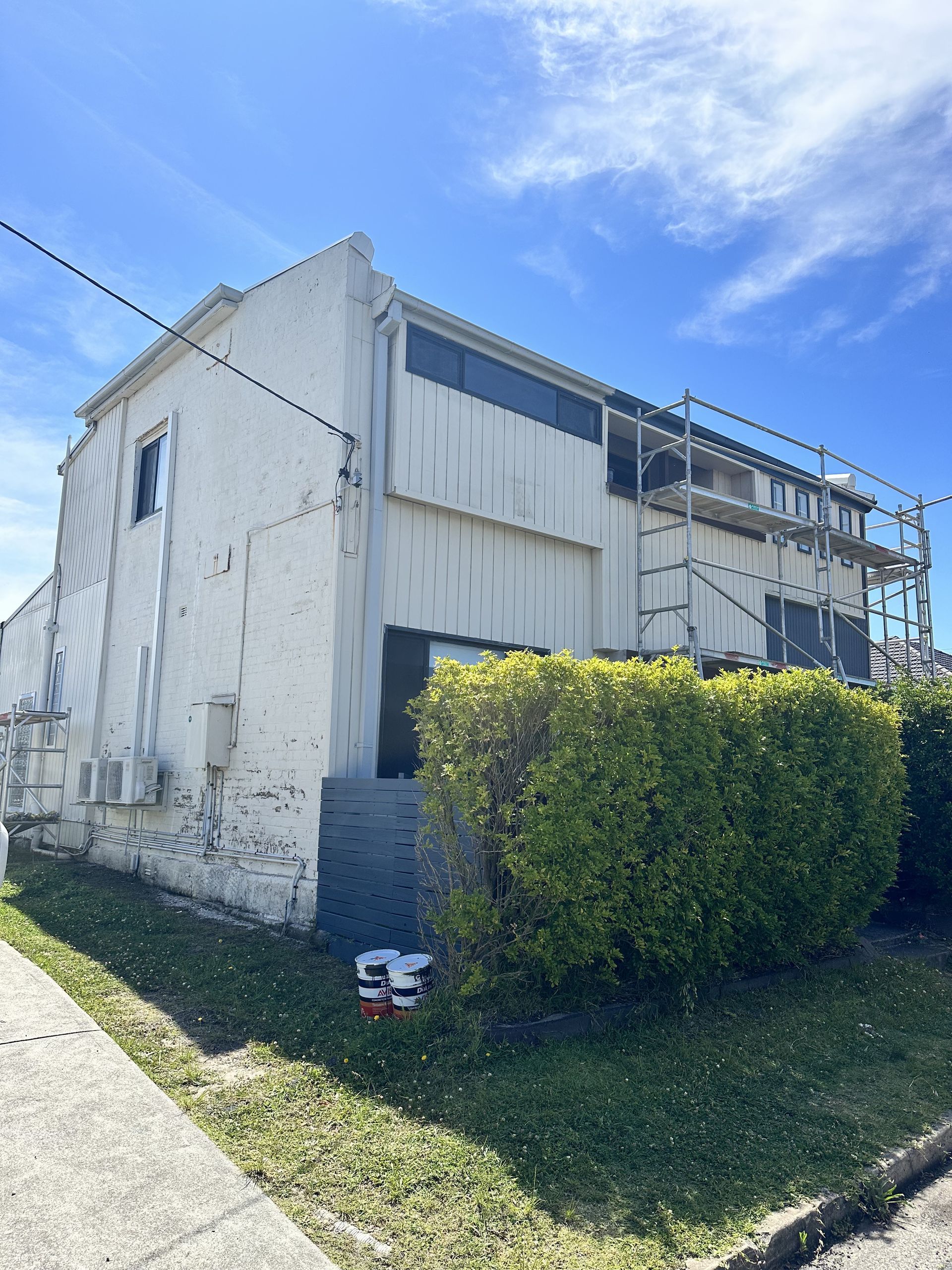 A white building with scaffolding on top of it is being painted — LMS Painting & Maintenance Pty Ltd In North Lambton, NSW
