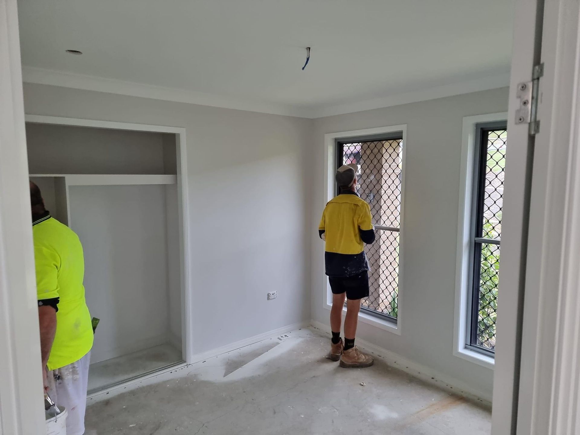 A Man Is Standing In An Empty Room Looking Out A Window — LMS Painting & Maintenance Pty Ltd In North Lambton, NSW
