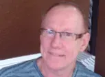 A close up of a man wearing glasses and a blue shirt.