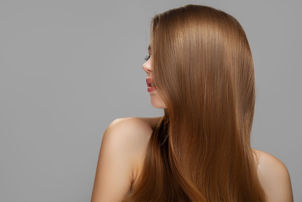 A woman with long brown hair is standing in front of a gray background.