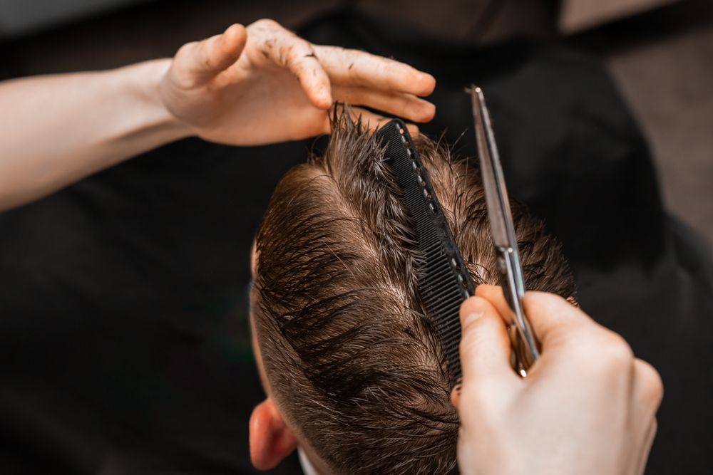 A man is getting his hair cut by a barber with scissors and a comb.