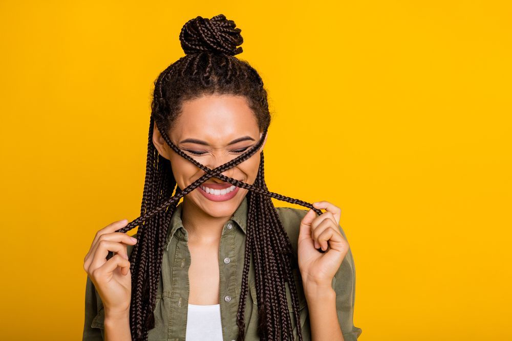 A woman with braids is covering her face with her hair.