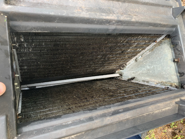 Dirty air conditioner evaporator coil inside a black plastic housing.