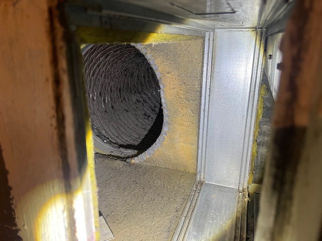 Inside view of a dusty air duct with a flexible vent tube; light illuminates the interior.