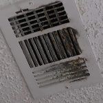 mold inspection services houston White air vent, dirty and discolored with grime, on a textured white wall.