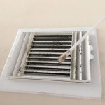 A person cleaning a dirty air vent with a cotton swab, removing dust and debris.