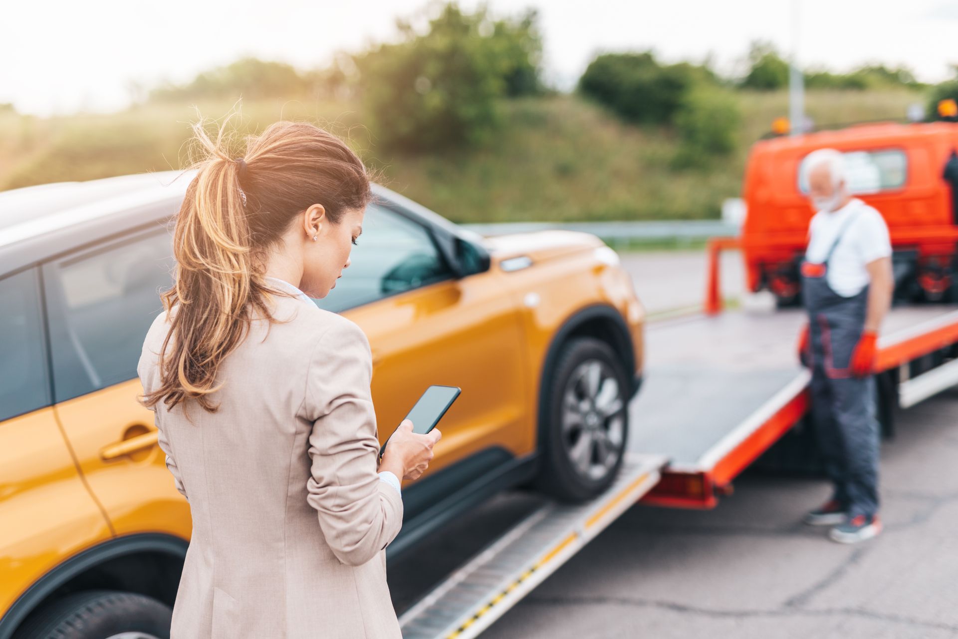 A woman is calling someone as a towing service is towing her car.