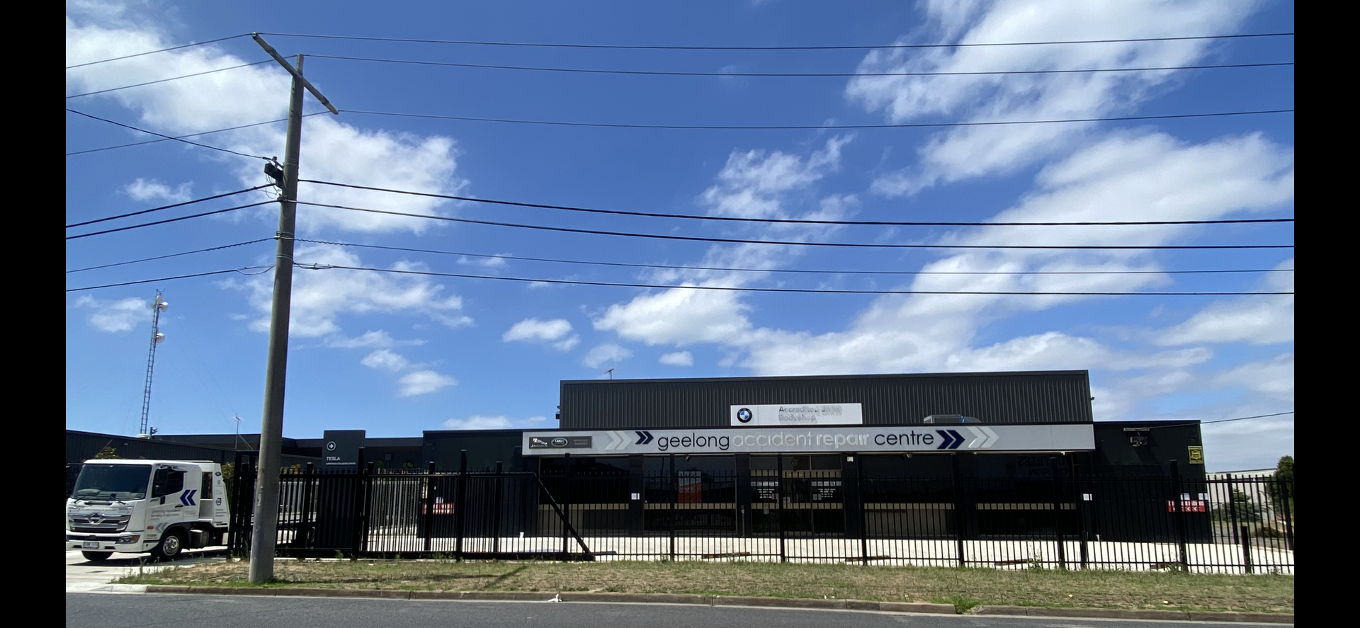 Exterior of a black building with signage under a blue sky with clouds, utility pole in the foreground.