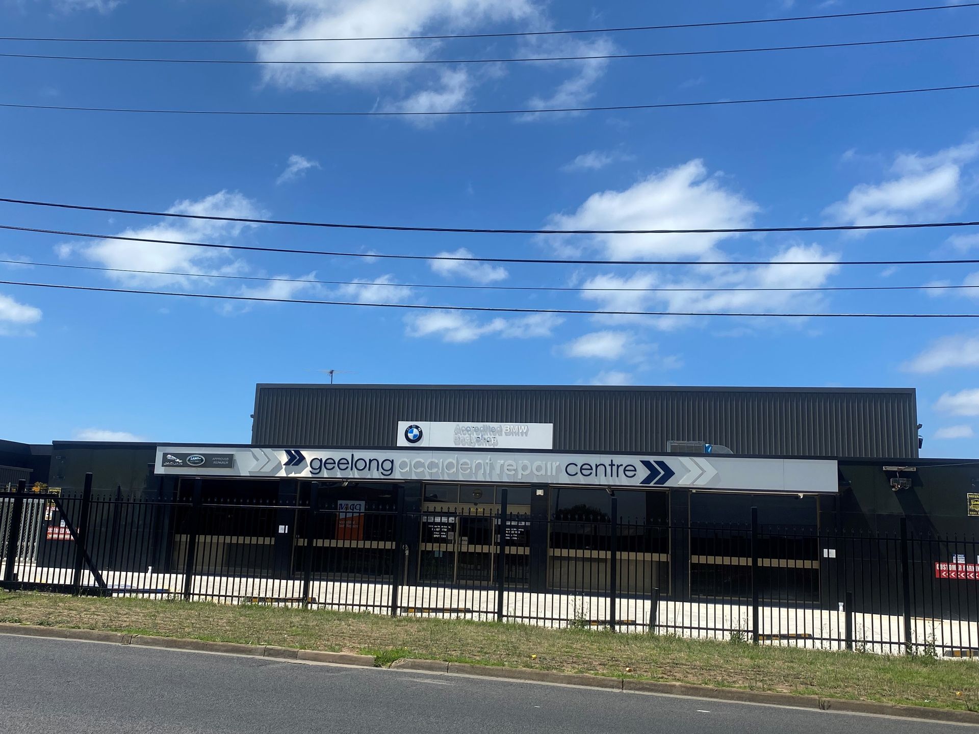 Building exterior with sign; black fence, blue sky, power lines.