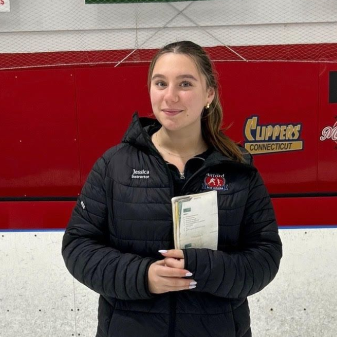 Person in a black jacket holding a certificate in front of a red-and-white rink wall.