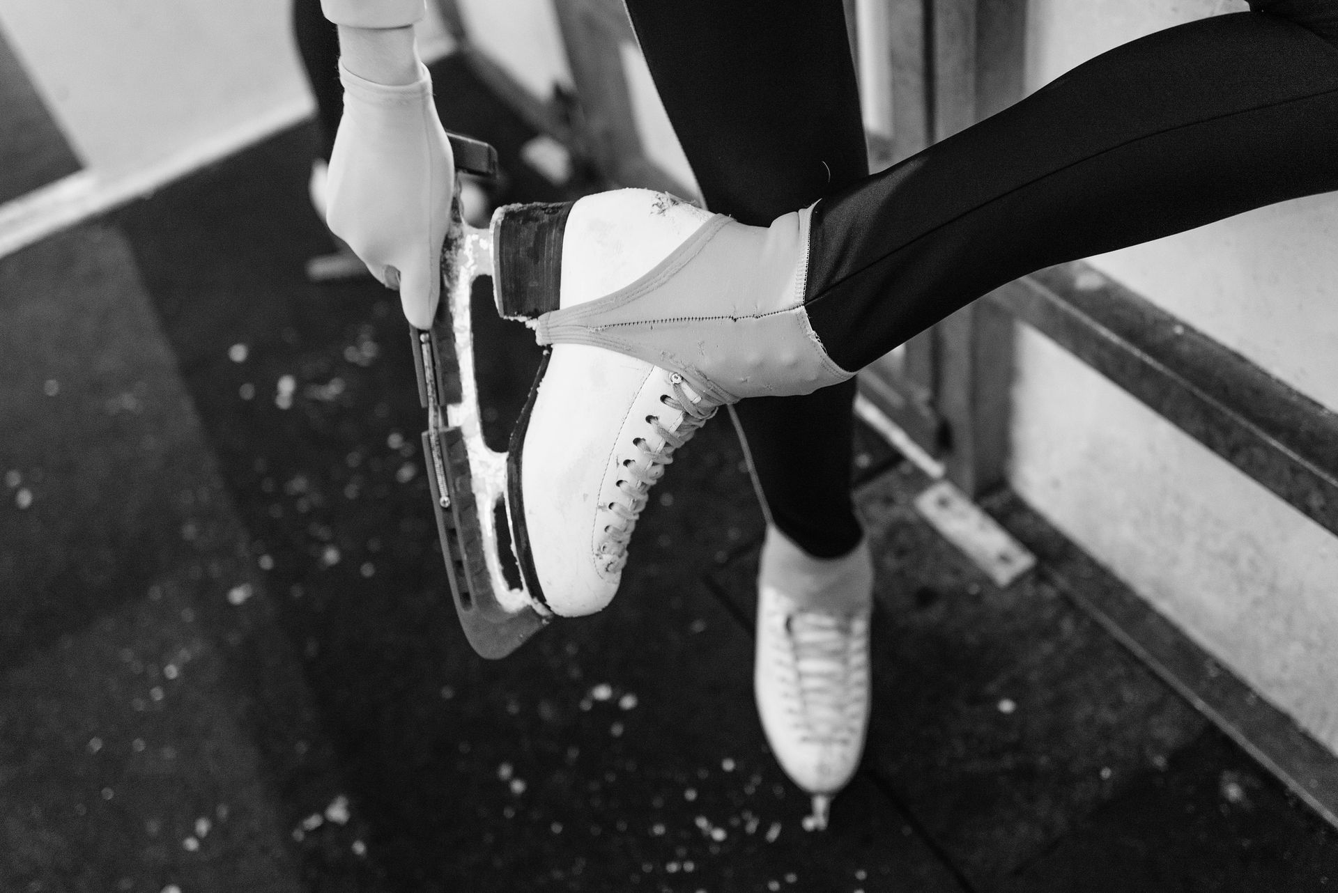Person tying a white ice skate on an ice rink bench