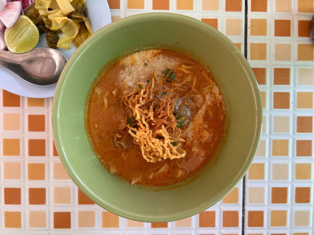 Bowl of khao soi (Northern Thai noodle soup) in green bowl, on a tiled surface with a side of condiments.