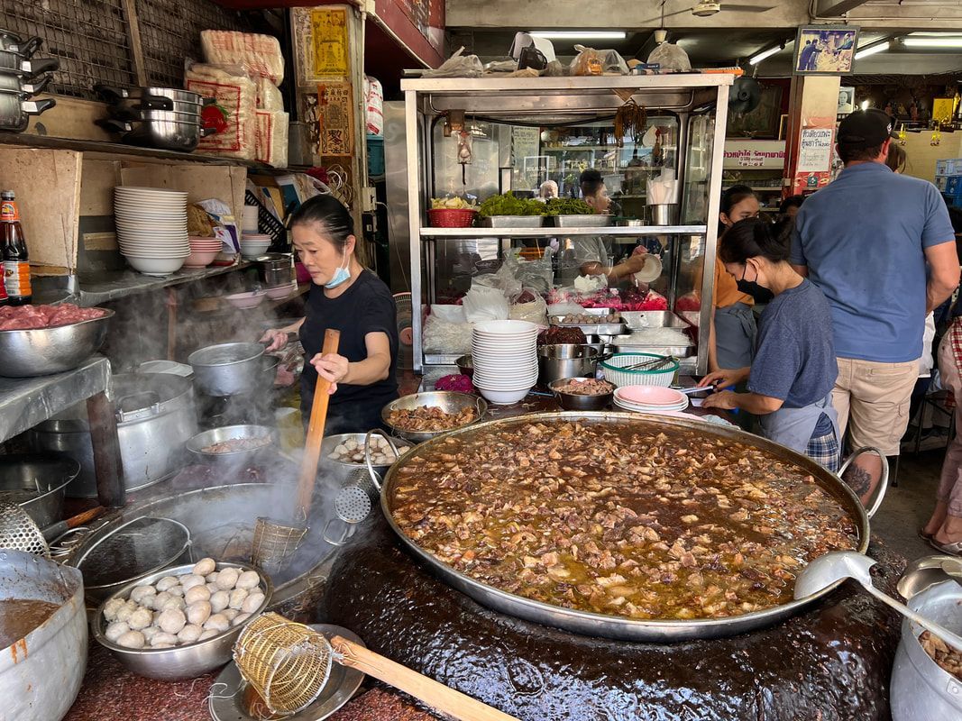 Street food stall in Thailand: Woman stirring a large pot of food.