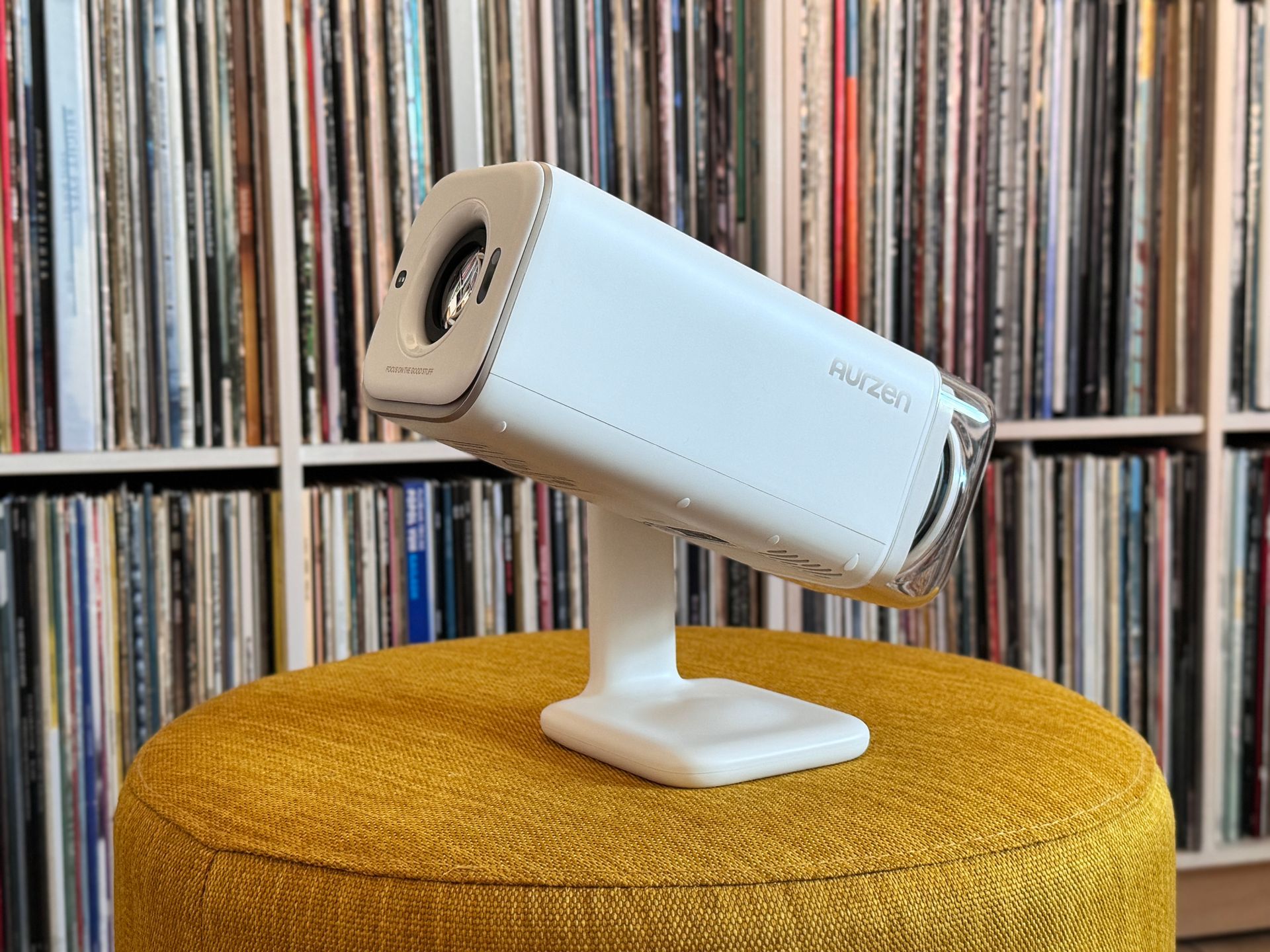 White security camera on a stand atop a mustard-yellow stool, with a blurred record shelf background