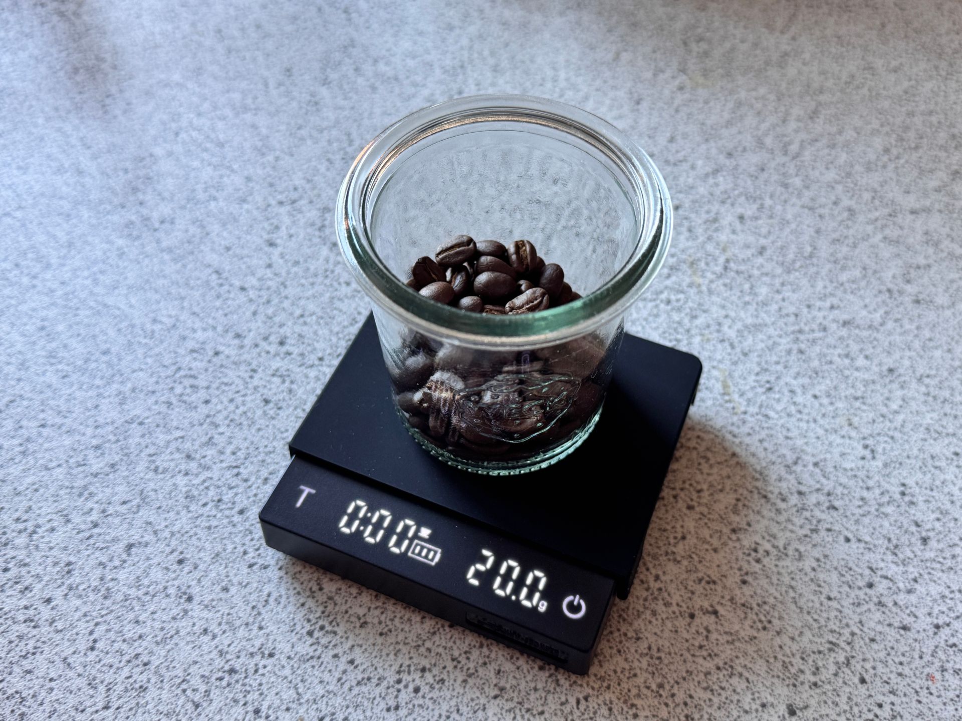 Glass jar of coffee beans on a black digital scale atop a gray countertop