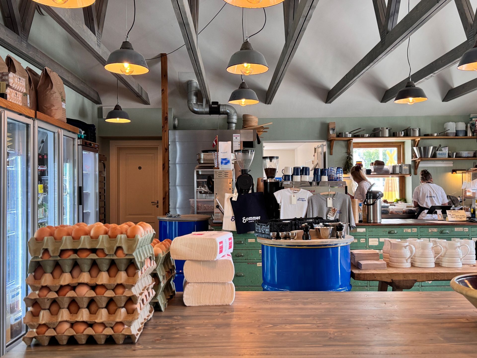 Interior of a cafe with stacked egg cartons, a counter, and staff preparing food under hanging lights.