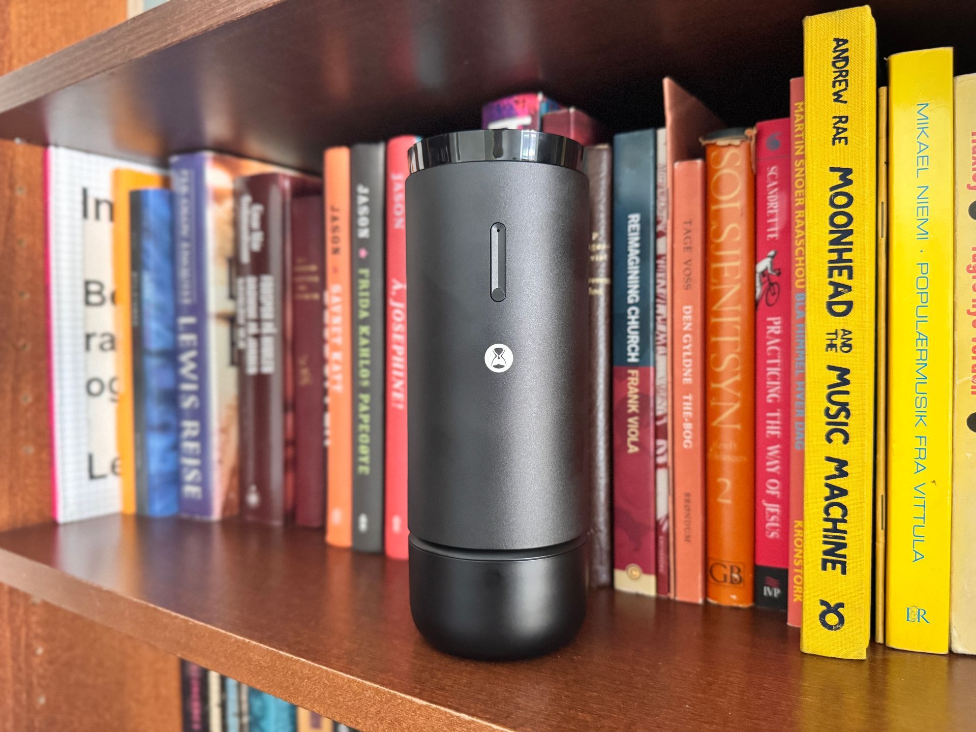 Black cylindrical coffee grinder on a wooden bookshelf with colorful books around it