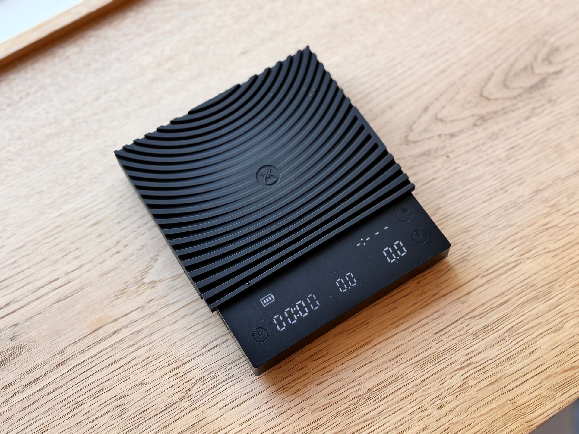 Black digital kitchen scale with blue display on a wooden table, beside round stone coasters