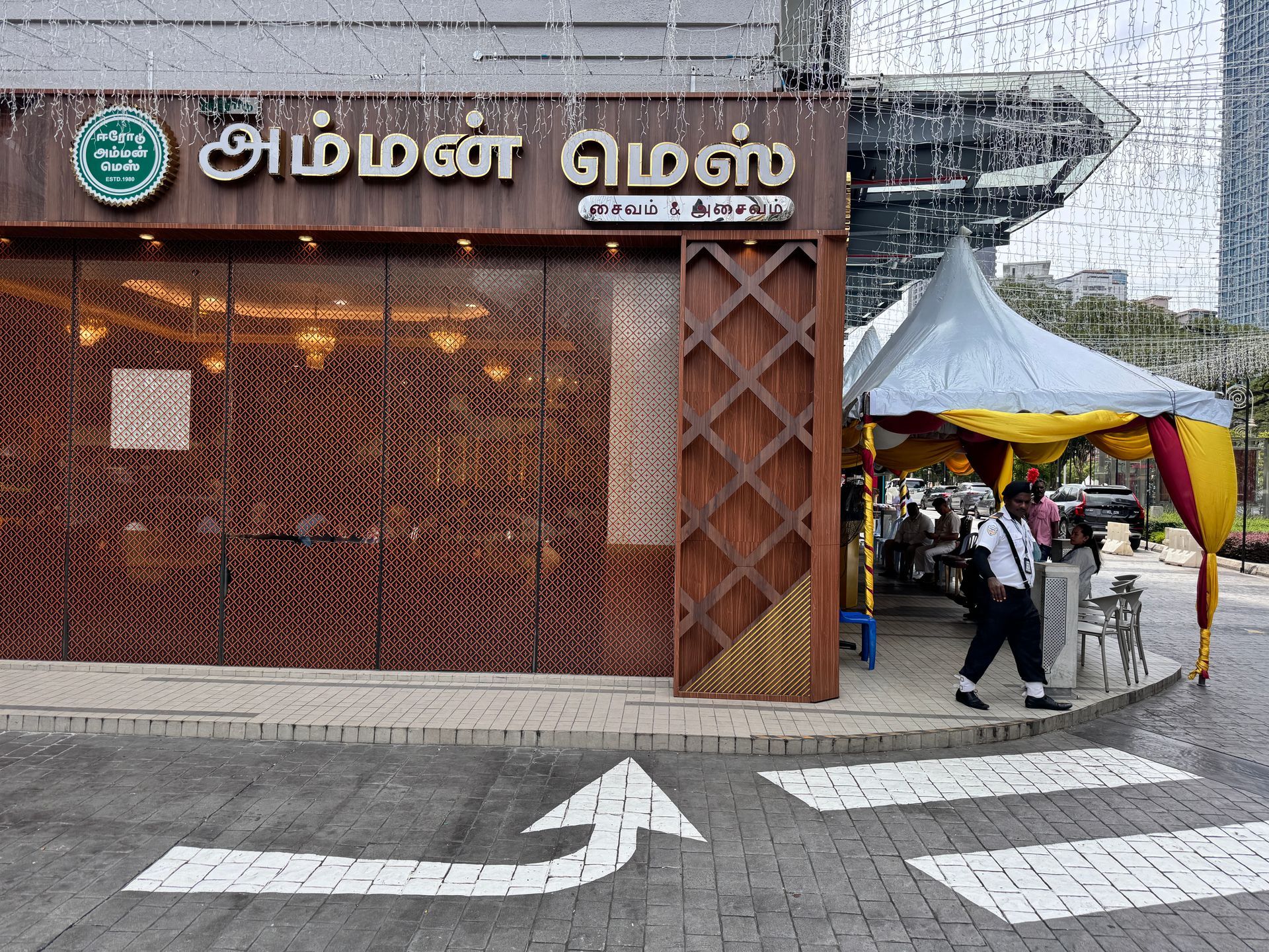 Restaurant exterior with two men seated, motorbike parked. Pink awning, white building.