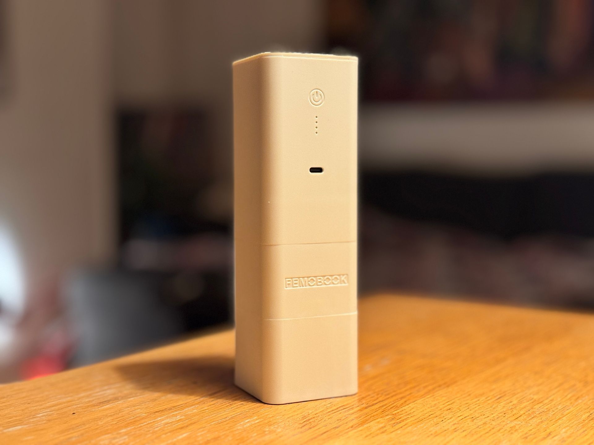 Tan rectangular device on a wooden surface, with a small hole and dots. Blurred background.