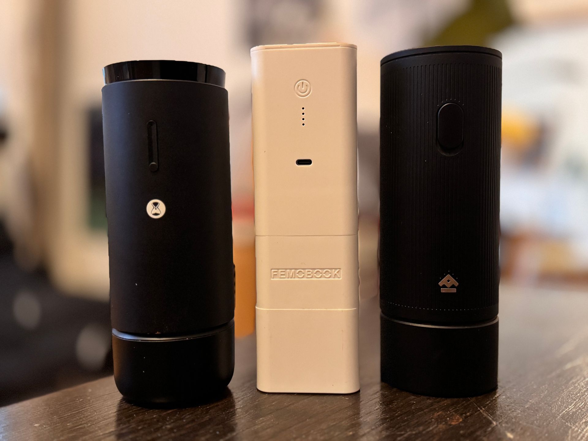 Four black coffee grinders of different designs on a counter, with a green container on the left.