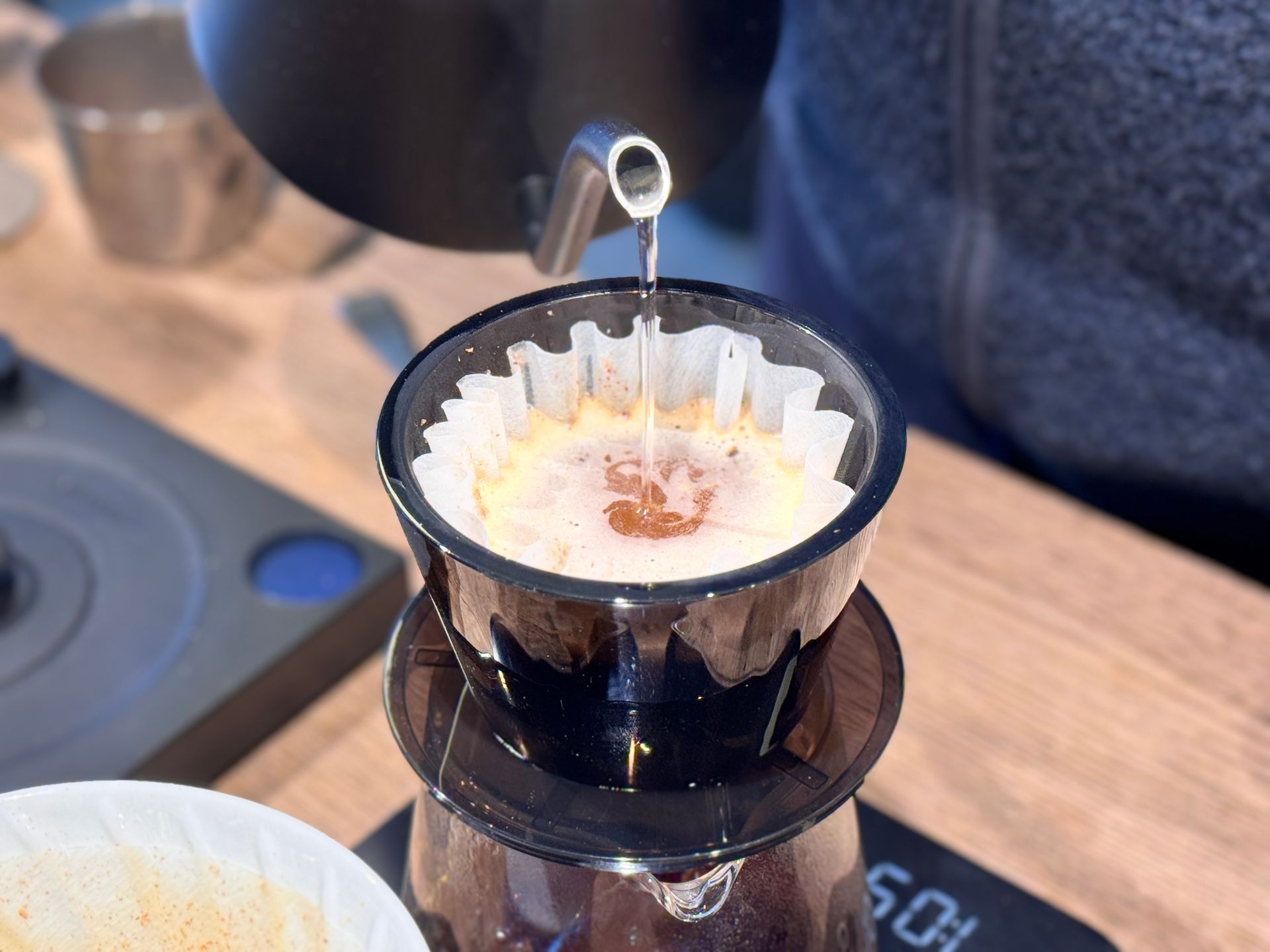 Pouring hot water from a black gooseneck kettle into a coffee pour-over filter with grounds.