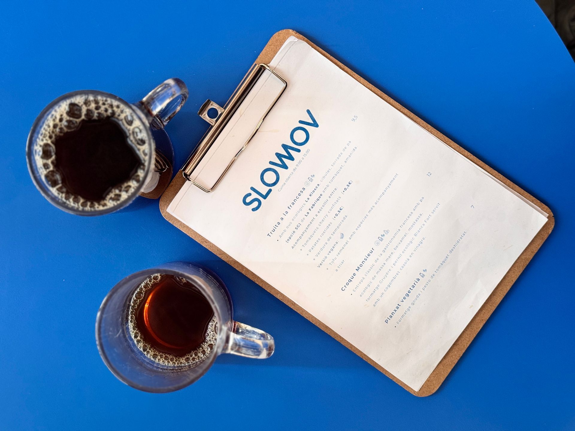 Overhead view of two coffee mugs beside a clipboard with a slow movement plan on a blue surface.