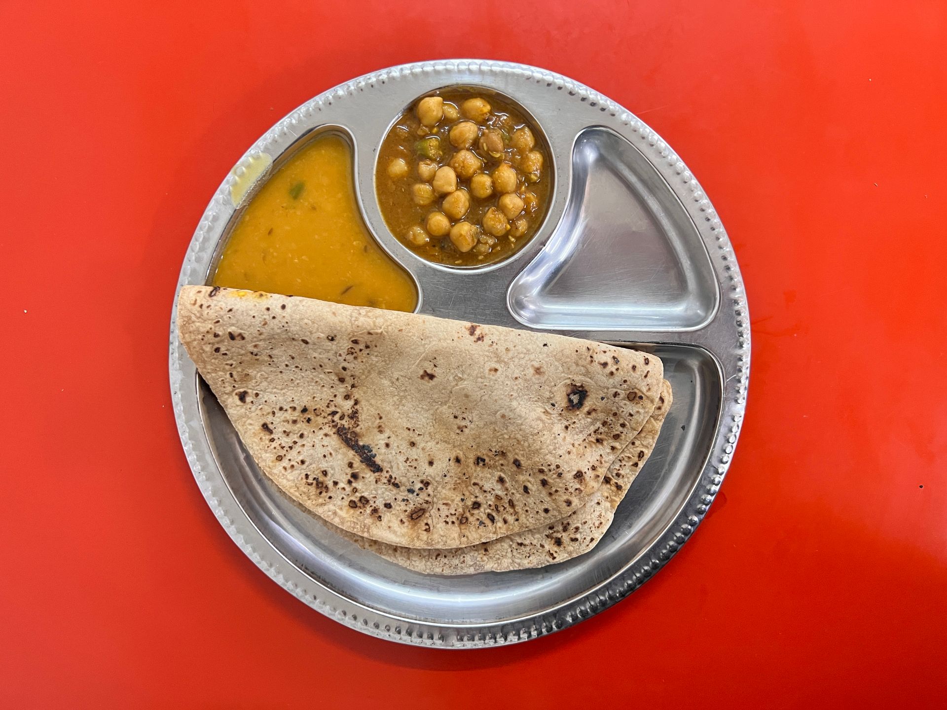 Plate of Indian food: chapati, chickpeas, lentil soup, on a red table.