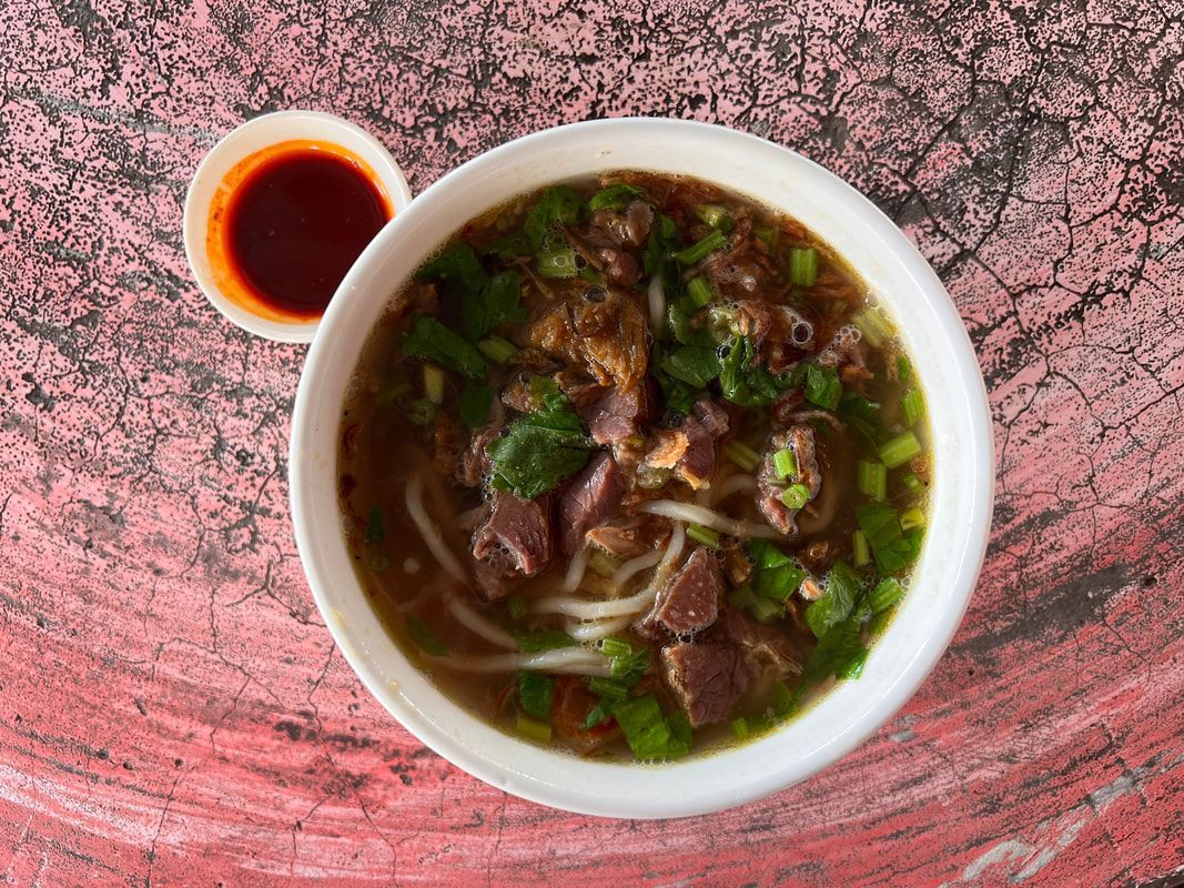 Bowl of beef noodle soup with red sauce on a red-marbled surface.