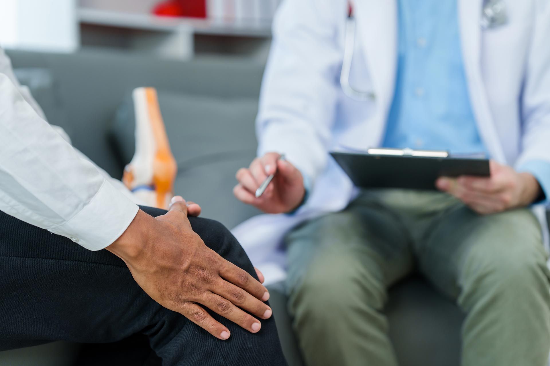 Patient seated during a medical consultation while a clinician holds a clipboard and takes notes. Patient seated during a medical consultation while a clinician holds a clipboard and takes notes.