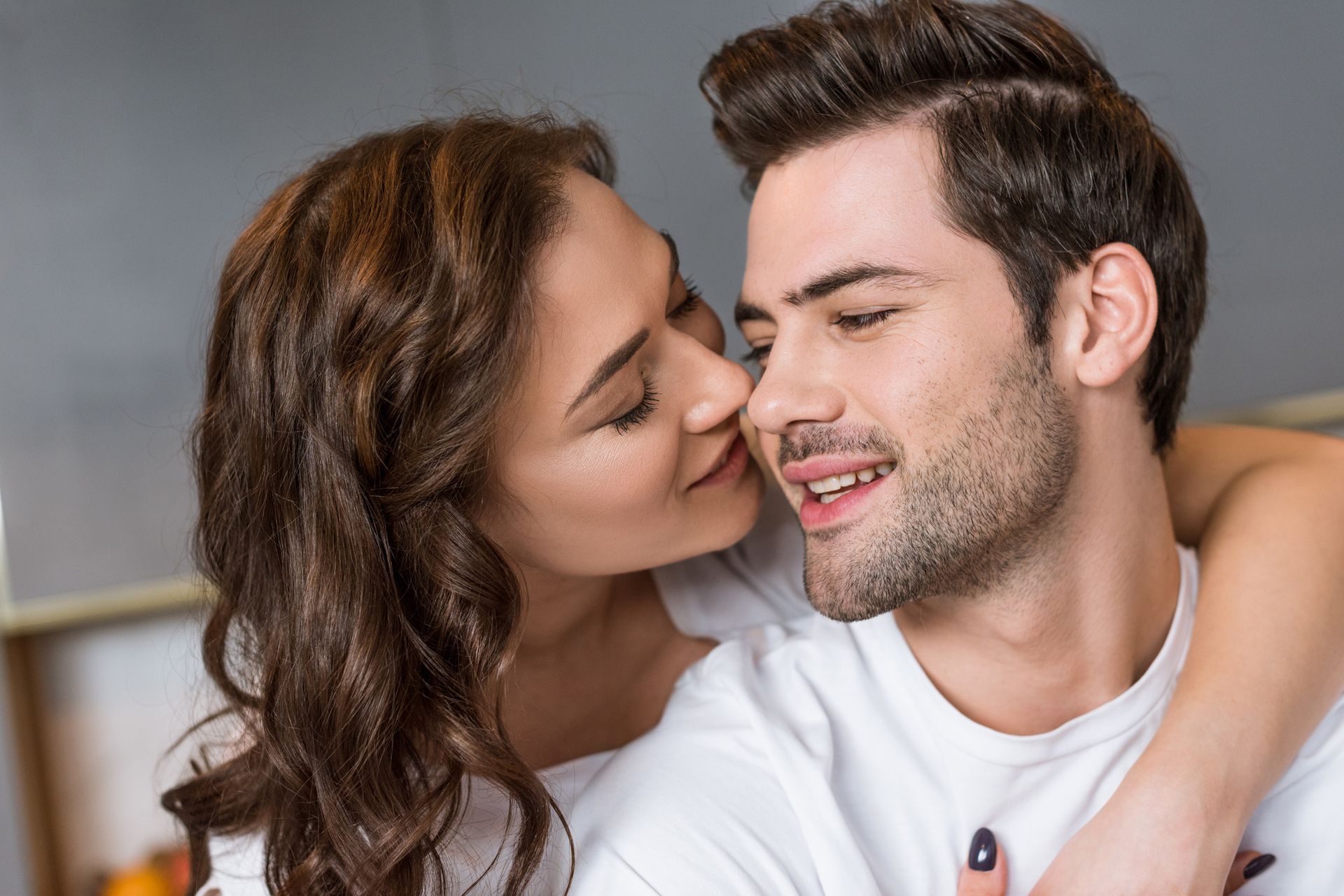 A woman is kissing a man on the cheek in a kitchen.