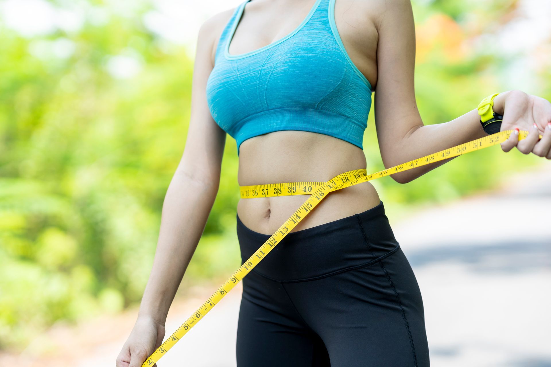 A woman is measuring her waist with a tape measure.
