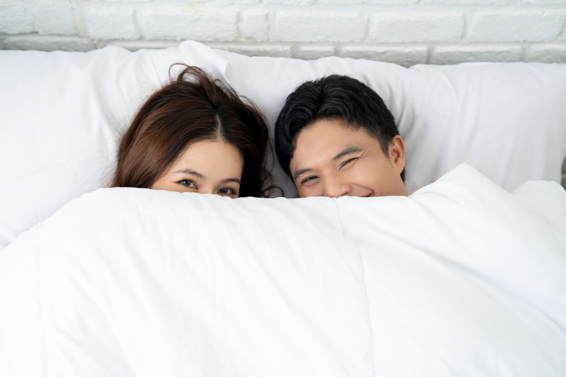 A man and a woman are laying in bed under a blanket.