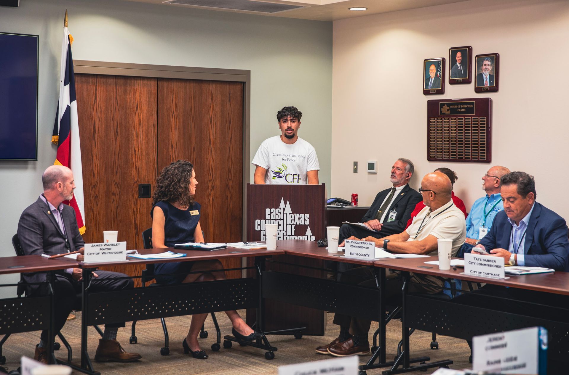 Board meeting in progress, with a speaker at the podium and members seated around conference tables.