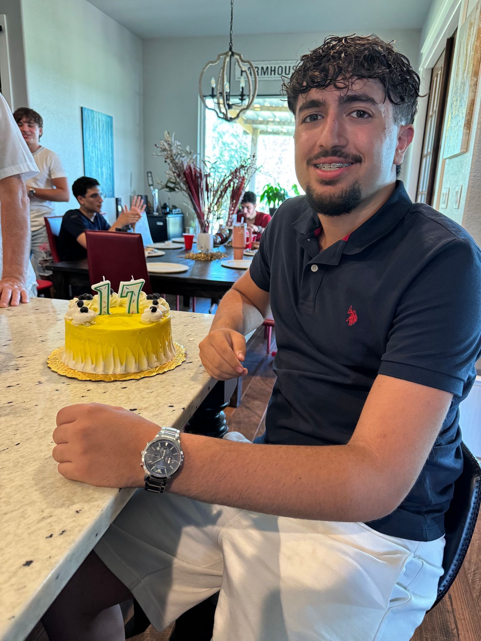 Man sitting at a table with a yellow cake in a bright dining room, smiling at the camera.
