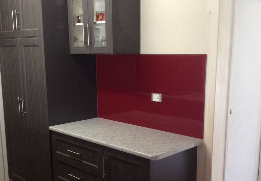 A kitchen with black cabinets and a red backsplash